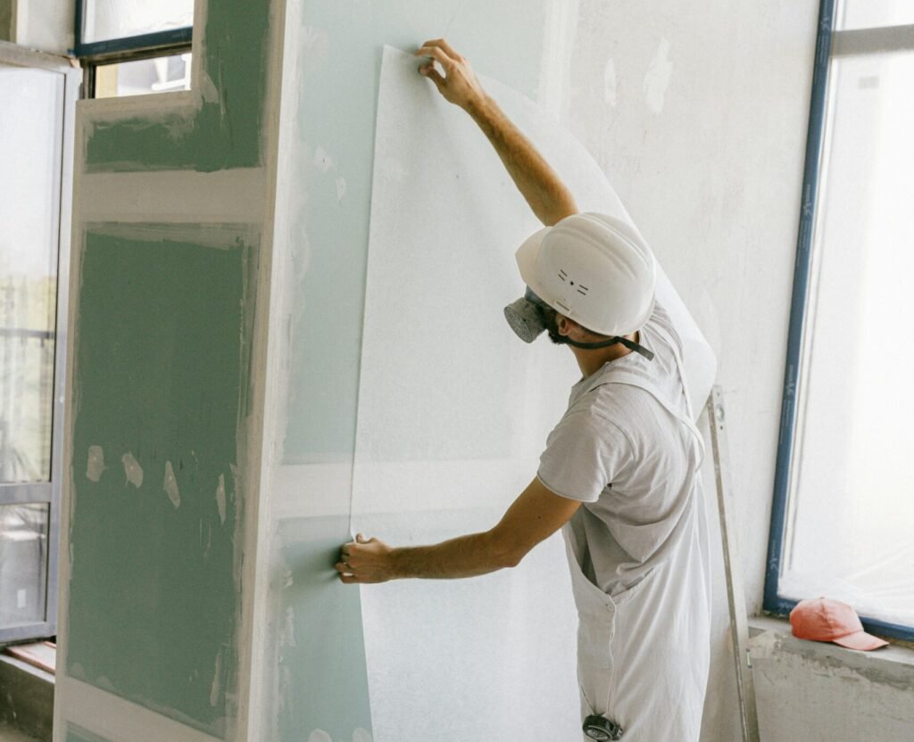 Construction worker in hard hat applying wallpaper inside a building under renovation.